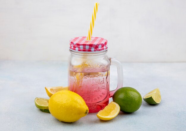 Vue latérale des citrons frais et colorés avec de l'eau dans un bocal en verre sur une surface blanche