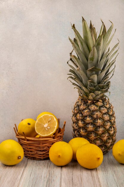 Vue latérale des citrons frais sur un seau avec des citrons et ananas isolé sur une table en bois gris sur une surface blanche