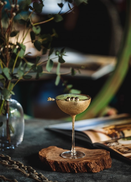 Vue latérale d'un cocktail d'alcool avec du kiwi dans un verre doré sur un support en bois