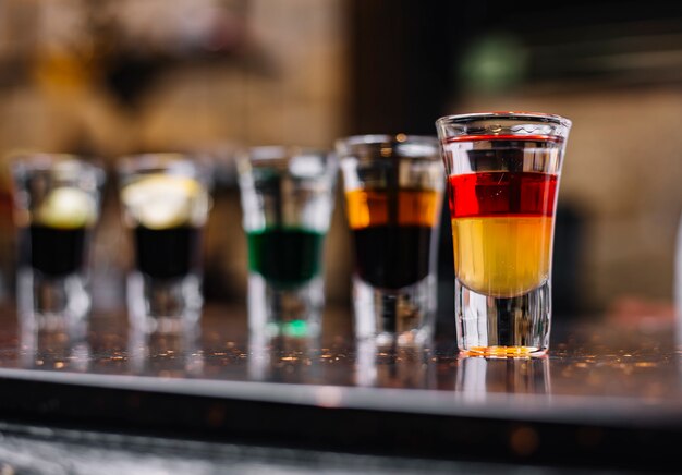Vue latérale de cocktails colorés dans des verres à liqueur sur un support de bar