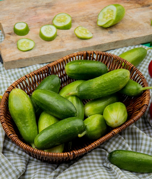 Photo gratuite vue latérale des concombres dans un panier avec du concombre en tranches sur une planche à découper sur un tissu écossais