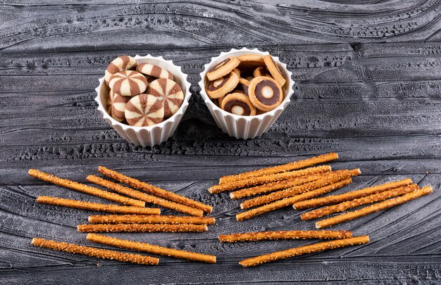 Vue latérale des cookies dans des bols et des craquelins sur horizontal sombre