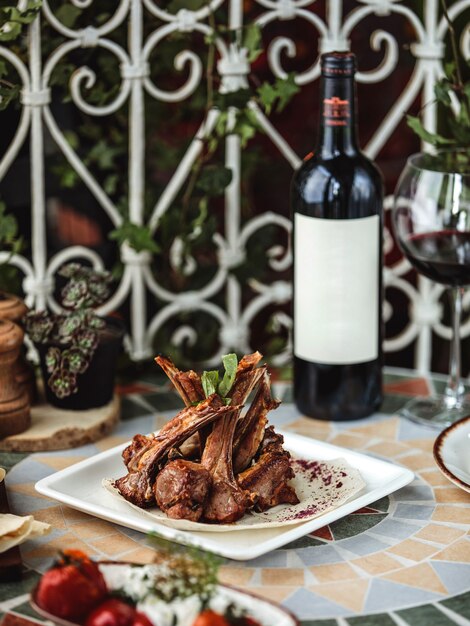 Vue latérale de la côte d'agneau kebab sur plaque servie avec une bouteille de vin rouge