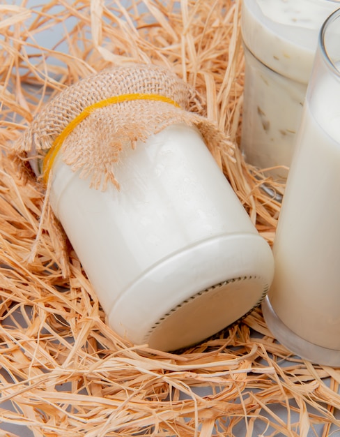 Photo gratuite vue latérale de la crème en pot avec verre de lait et soupe de yaourt sur la surface de la paille