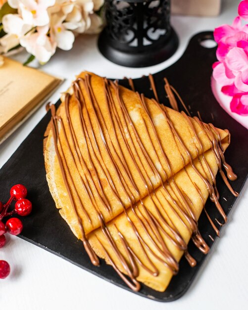 Vue latérale de la crêpe avec du sirop de cacao au chocolat sur une planche à découper en bois