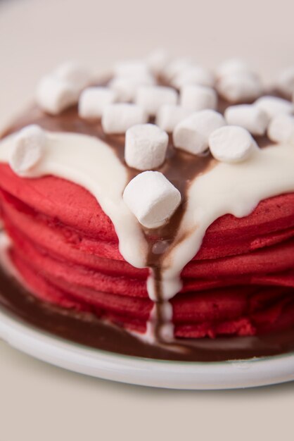 Vue latérale de crêpes rouges avec de la crème et des guimauves en plaque isolé