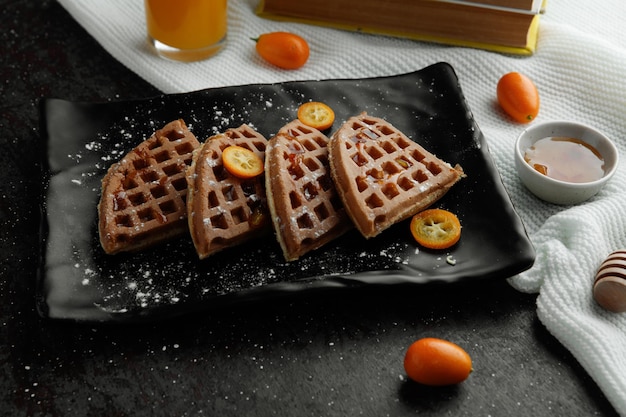 Vue latérale des crêpes avec des tranches de kumquat dans une assiette et de la confiture de jus d'orange sur un tissu sur fond noir