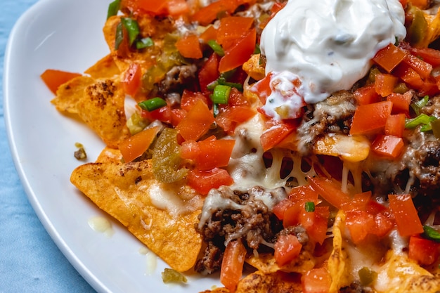 Photo gratuite vue latérale croustilles nachos tortilla avec viande hachée grillée tomate oignon de printemps fromage tomate piment jalapeño et crème sure sur le dessus