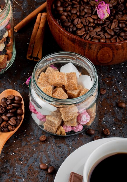 Vue latérale des cubes de sucre brun dans un bocal en verre et des grains de café dans un bol sur fond noir