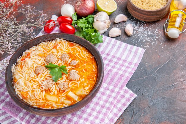 Vue latérale d'une délicieuse soupe au poulet avec des nouilles vertes et une cuillère sur une serviette rose bouteille d'huile à l'ail tomates citron sur fond sombre