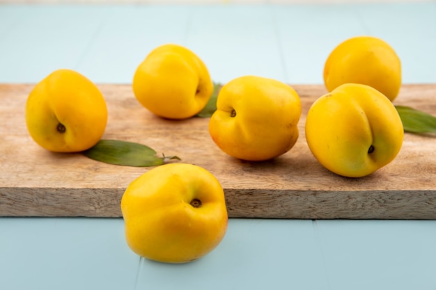 Vue latérale de délicieuses pêches jaunes fraîches sur une planche de cuisine en bois sur fond bleu