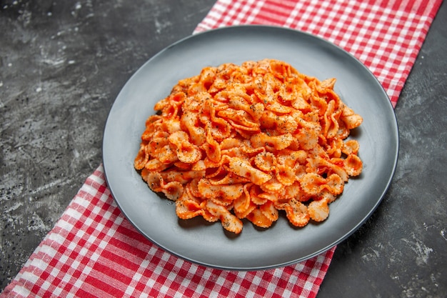 Vue latérale d'un délicieux repas de pâtes sur une assiette noire pour le dîner sur une serviette dénudée rouge sur fond sombre