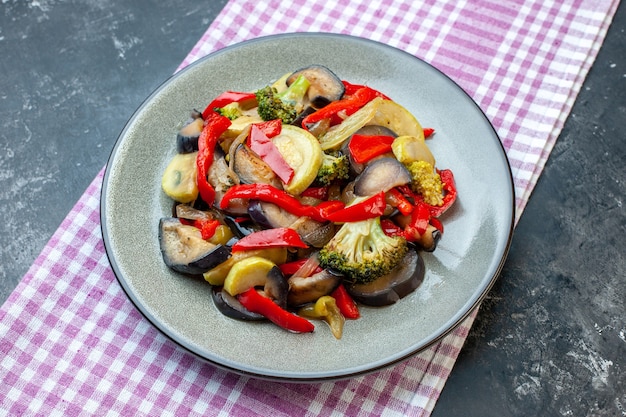 Vue latérale d'un délicieux repas végétarien sur une assiette sur une serviette à rayures violettes sur fond sombre