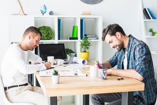 Vue latérale de deux jeunes entrepreneurs assis au bureau