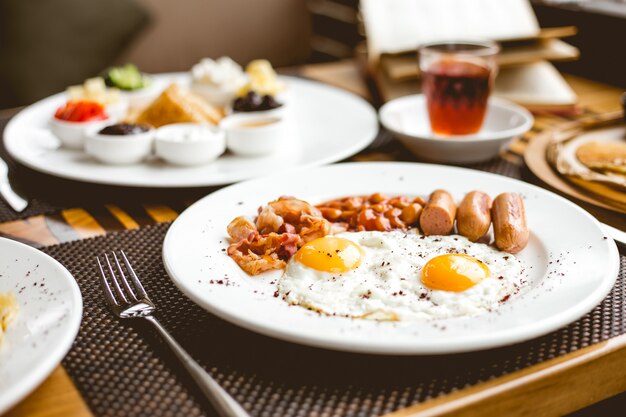 Vue latérale deux œufs sur le plat avec des haricots et des lardons de saucisses sur une plaque