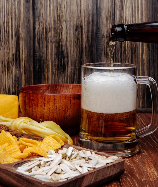 Vue latérale de diverses collations de bière salée sur un plateau en bois et verser de la bière dans une tasse sur bois rustique