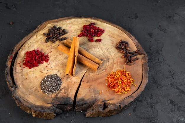 Vue latérale de diverses épices safran piment en poudre poivre noir et bâtons de cannelle sur une planche de bois ronde