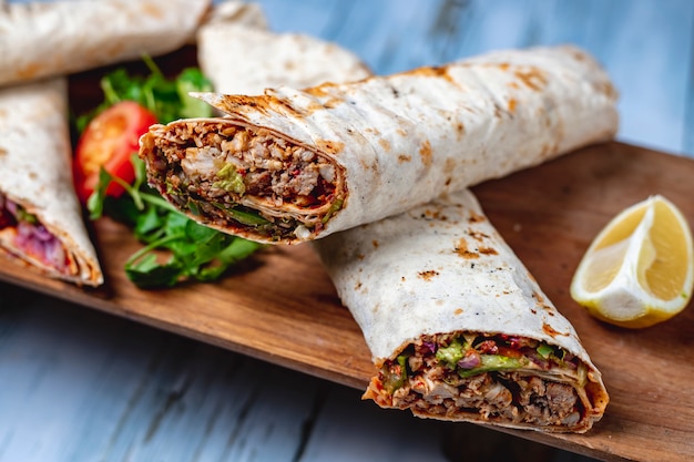 Vue latérale doner de poulet avec des verts concombre sauce tomate concombre oignon rouge en pita et tranche de citron sur une planche