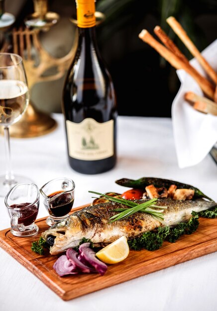 Vue latérale du bar cuit au four avec des légumes oignon rouge citron sur wodden board