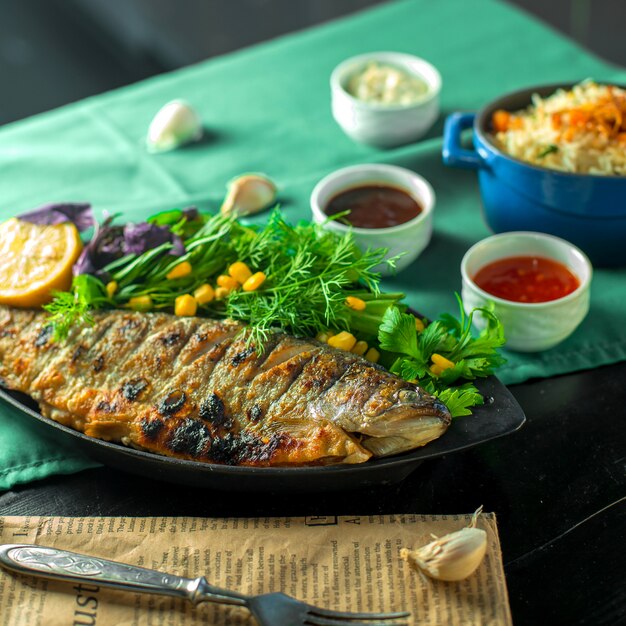 Vue latérale du bar cuit au four servi avec des herbes fraîches et des sauces sur la table