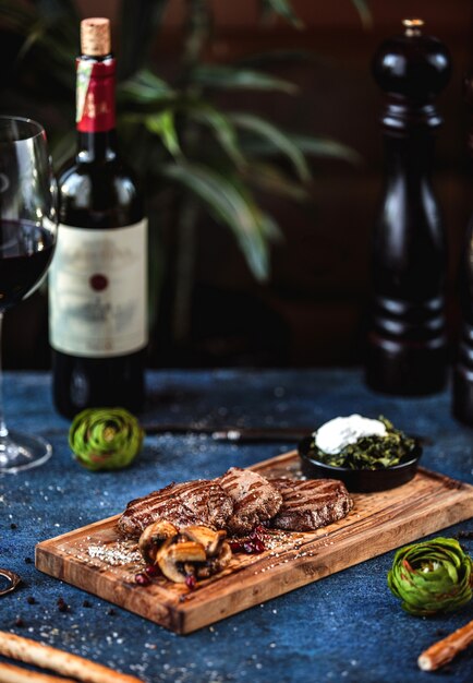 Vue latérale du boeuf grillé aux champignons et sauce sur planche de bois