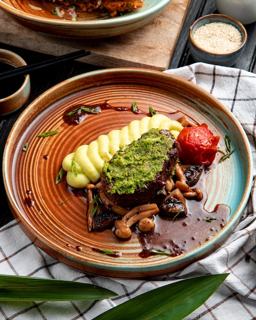 Vue latérale du boeuf grillé avec purée de pommes de terre tomates champignons et sauce avocat dans une assiette sur nappe à carreaux