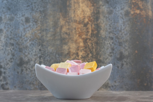 Vue latérale du bol blanc plein de bonbons sucrés sur fond gris.