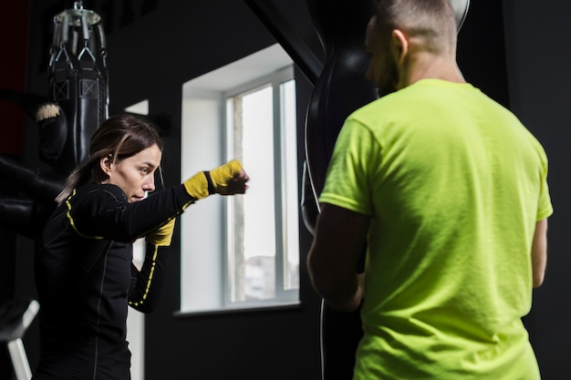 Vue latérale du boxeur féminin pratiquant avec un entraîneur masculin en t-shirt