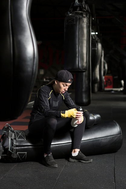 Vue latérale du boxeur féminin tenant le flacon à côté des sacs de boxe