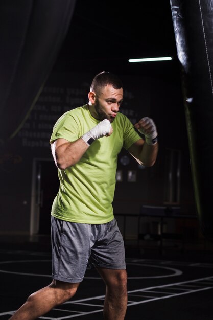 Vue latérale du boxeur masculin portant un t-shirt et un short pratiquant avec un sac de boxe