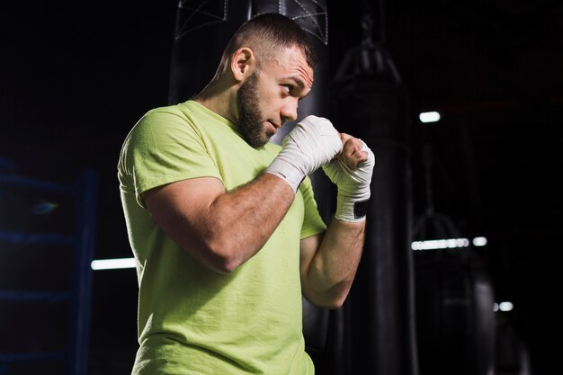 Vue latérale du boxeur masculin en t-shirt pratiquant dans la salle de gym