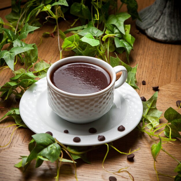 Vue latérale du café turc avec des grains de café et une branche de raisin dans une tasse sur une table en bois