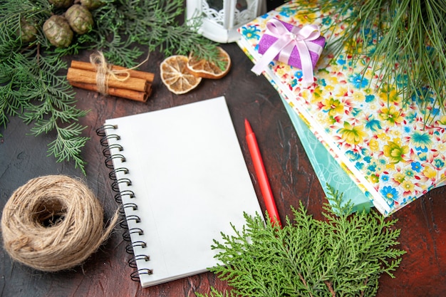 Vue latérale du cahier fermé avec stylo limes à la cannelle une boule de branches de sapin de corde et de livres sur fond sombre