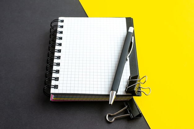 Vue latérale du cahier à spirale sur livre et stylos sur fond jaune noir avec espace libre