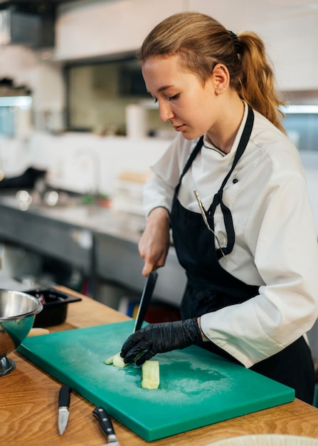 Vue latérale du chef féminin couper les légumes