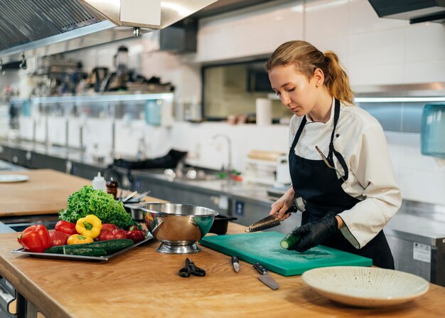 Vue latérale du chef féminin dans la cuisine, trancher les légumes
