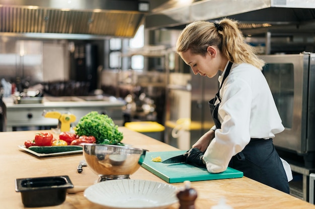 Vue latérale du chef féminin avec gant, trancher les légumes dans la cuisine