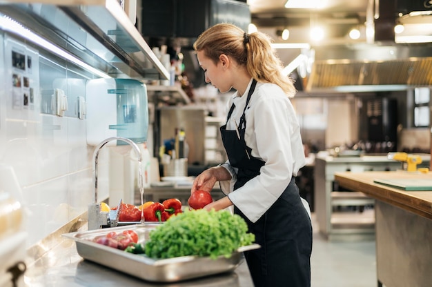 Vue latérale du chef féminin laver les légumes dans la cuisine