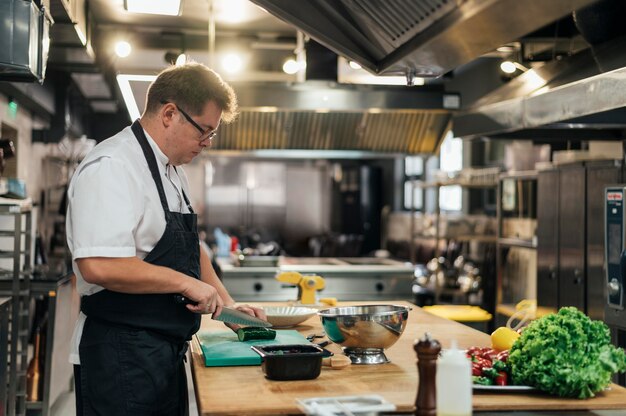 Vue latérale du chef masculin dans la cuisine, préparer des légumes