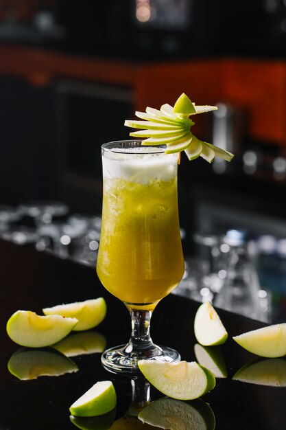 Vue latérale du cocktail aux pommes vertes décoré de pommes en tranches dans un verre au bar background