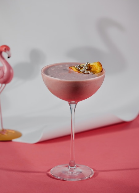 Vue latérale du cocktail de fruits roses décoré avec une tranche d'orange séchée dans un verre sur le mur rose