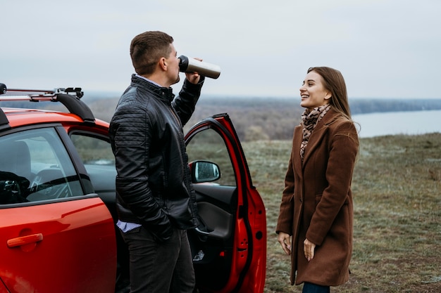 Vue latérale du couple à côté de la voiture de boire du thermos