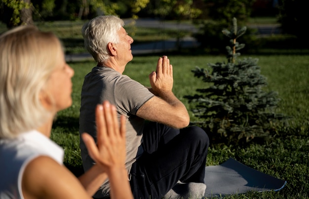 Vue latérale du couple de personnes âgées pratiquant le yoga à l'extérieur