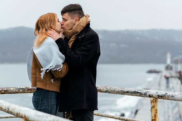 Vue latérale du couple s'embrassant au bord du lac en hiver
