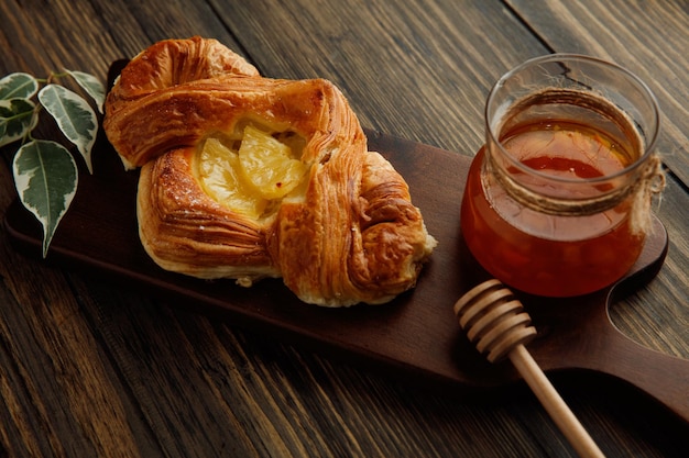 Vue latérale du croissant et pot de confiture en verre avec des feuilles sur une planche à découper sur fond de bois