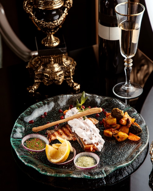 Vue latérale du filet de poisson au four garni d'épices et de sauce aux légumes sur une assiette avec un verre de vin blanc sur la table