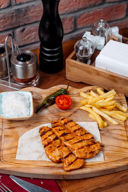 Vue latérale du filet de poulet grillé avec des frites sur une planche de bois