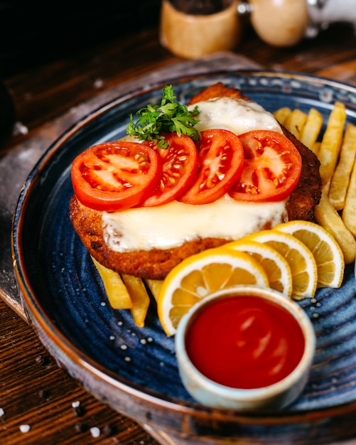 Photo gratuite vue latérale du filet de poulet pané frit avec du fromage servi avec des tranches de ketchup de citrons et tomates frites sur rustique