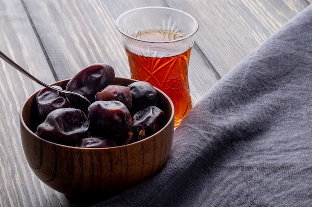 Vue latérale du fruit de datte séché sucré dans un bol avec un verre de thé armudu sur un rustique en bois