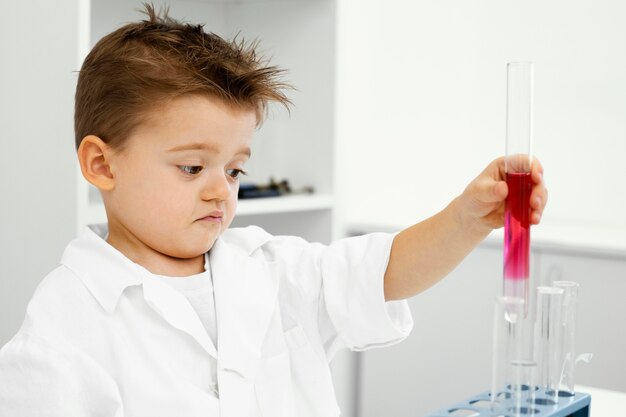 Vue latérale du garçon scientifique dans le laboratoire avec des tubes à essai faisant des expériences